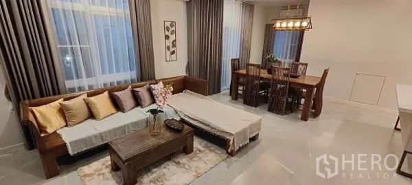Detached House for rent in Prawet, Bangkok - Open-plan living and dining area with wooden sofa, rug, and six-seat dining set.