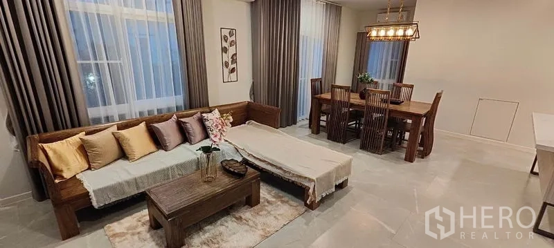 Detached House for rent in Prawet, Bangkok - Open-plan living and dining area with wooden sofa, rug, and six-seat dining set.