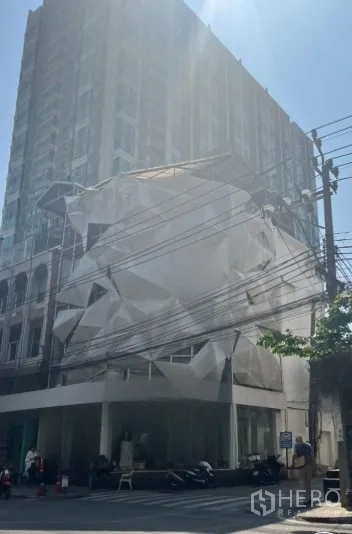 店屋 for rent in Watthana, Bangkok - 转角店屋外观，大片玻璃门面与白色外立面覆盖，晴天街景。