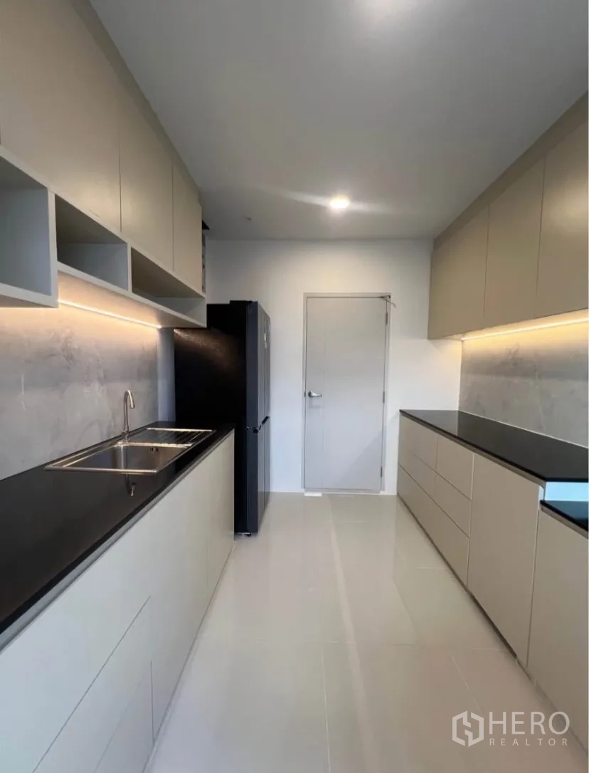 独栋房屋 for rent in Bang Phli, Samut Prakan - 现代走廊式厨房，黑色石材台面，充足橱柜，橱柜下灯光与冰箱。