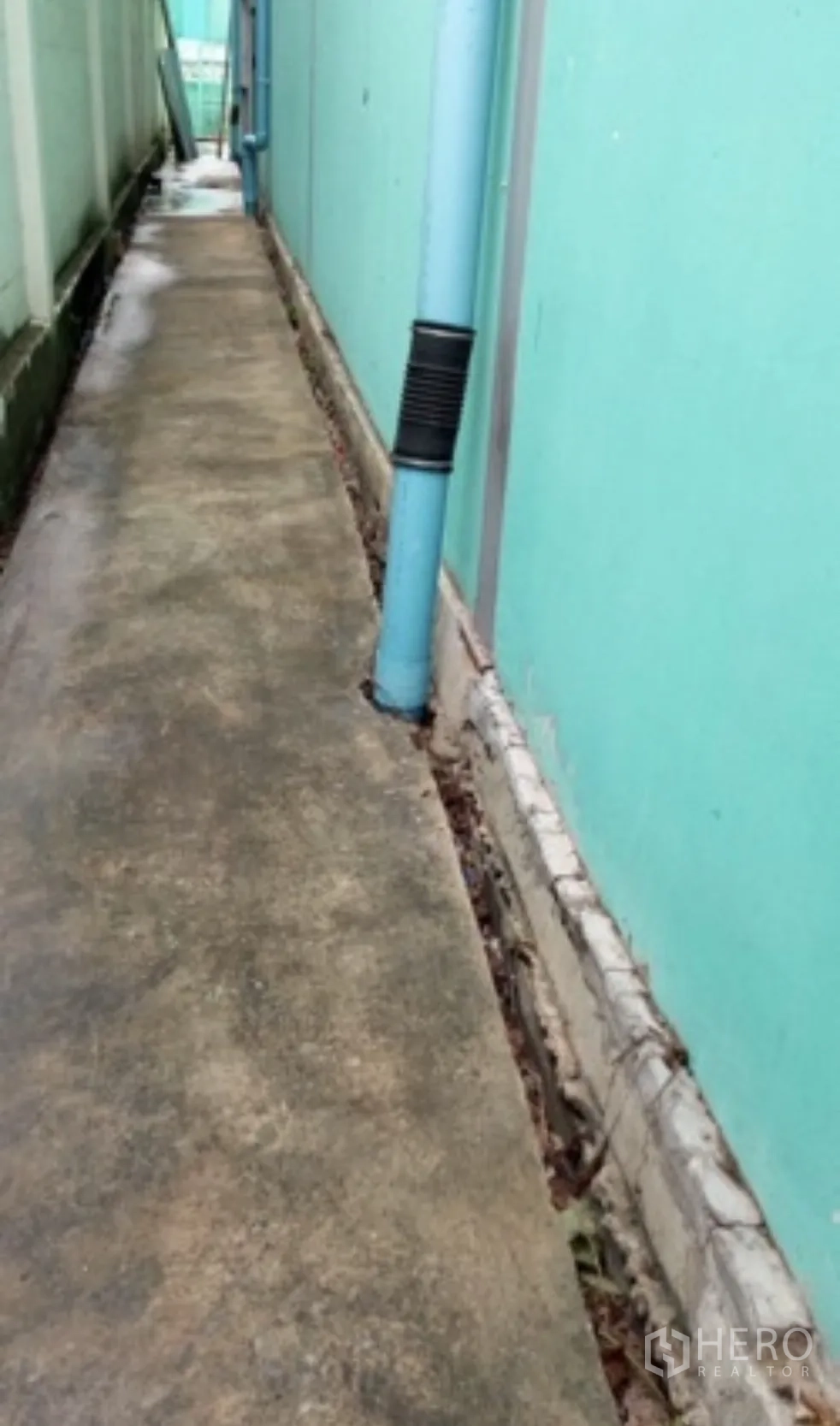 Warehouse for rent in Pak Kret, Nonthaburi - Exterior side path along the warehouse wall with visible utility pipes.