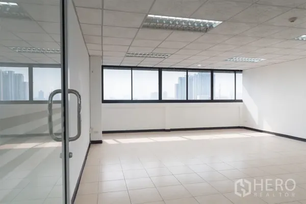 Office Space for rent in Din Daeng, Bangkok - Bright empty office with tiled floors, drop‑ceiling lights, and wide windows offering Bangkok skyline views, seen through a glass door.
