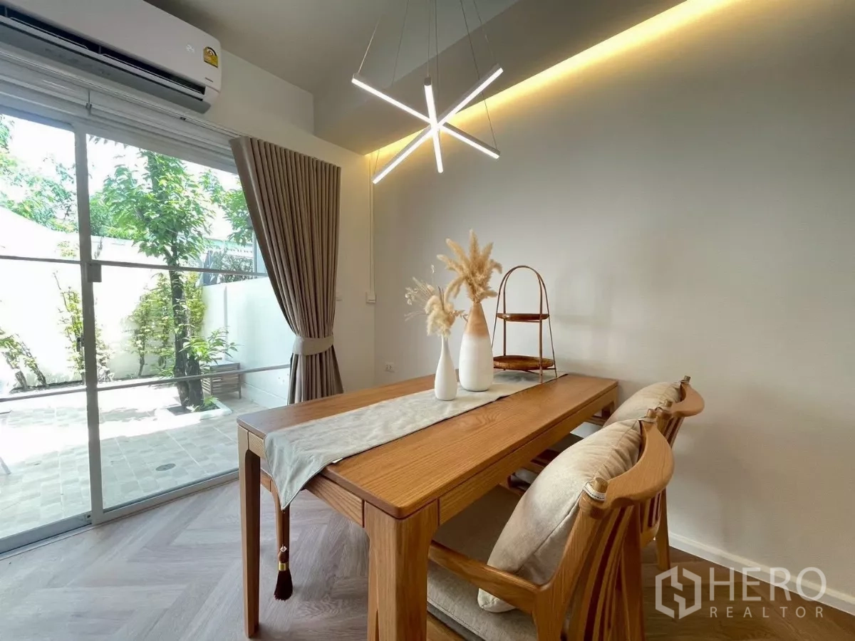 联排别墅 出租在Prawet, Bangkok - 餐桌下方现代吊灯，紧邻通向后院的大推拉窗。