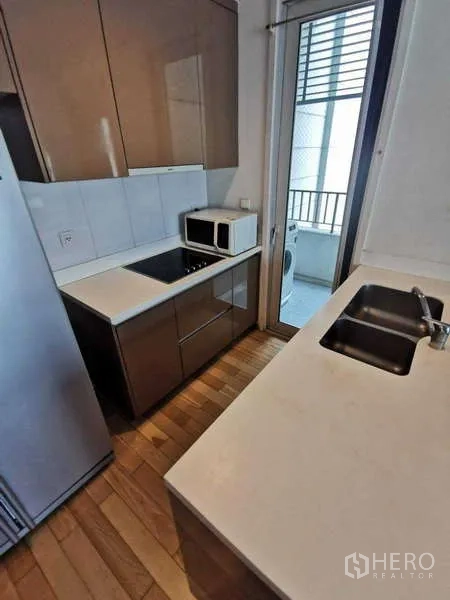 Condominium for rent in Khlong Toei, Bangkok - Kitchen island with double sink facing the cooktop and storage.