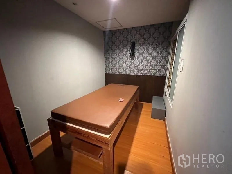 Retail Space for rent - Compact treatment room with massage bed, wood flooring, patterned wallpaper and soft lighting.