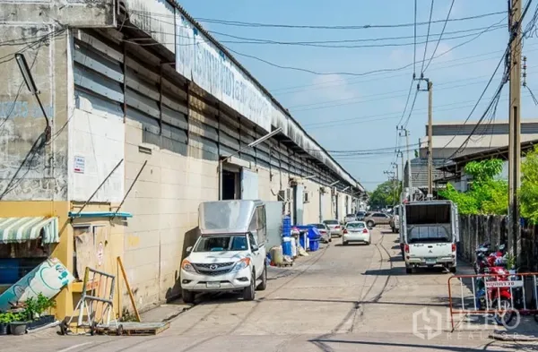 Warehouse for rent in Bang Phli, Samut Prakan - Service lane lined with warehouse bays, loading doors and parked delivery vehicles in an industrial estate.
