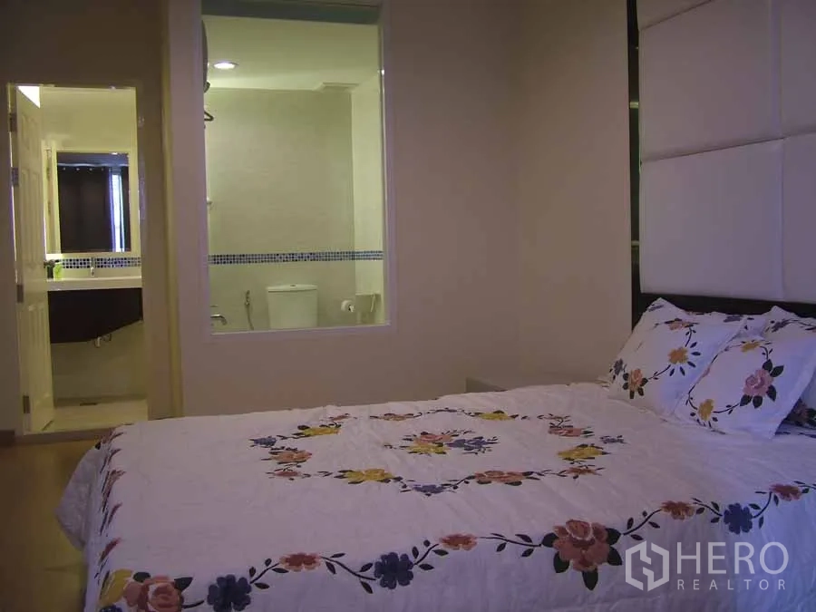 公寓 出租或出售在Watthana, Bangkok - 卧室铺花卉床品，通过内窗可见套内卫浴。