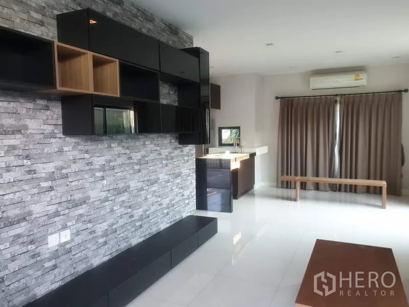 Detached House for sale in Bang Kapi, Bangkok - Bright living area featuring a stone feature wall, built-in shelving and full-length curtains.