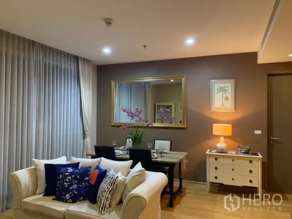 公寓 出租在Watthana, Bangkok - 温馨客餐厅，奶油色沙发、摆好餐具的餐桌、大墙镜与柔和灯光。