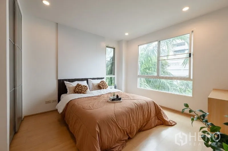 公寓 出售在Watthana, Bangkok - 转角主卧，大窗采光充足，绿树景观与暖色床品。