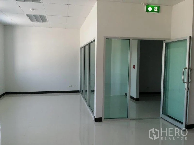 Warehouse for rent in Samut Prakan - Glass-partitioned office corridor with sliding doors and an illuminated emergency exit sign.