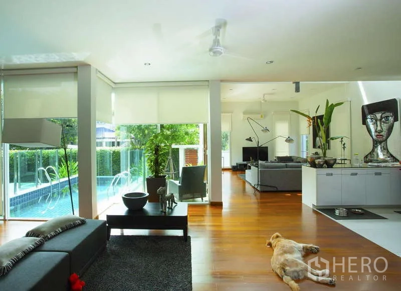 Detached House for rent in Lat Phrao, Bangkok - Open-plan living area with pool views, hardwood floors, and expansive windows.
