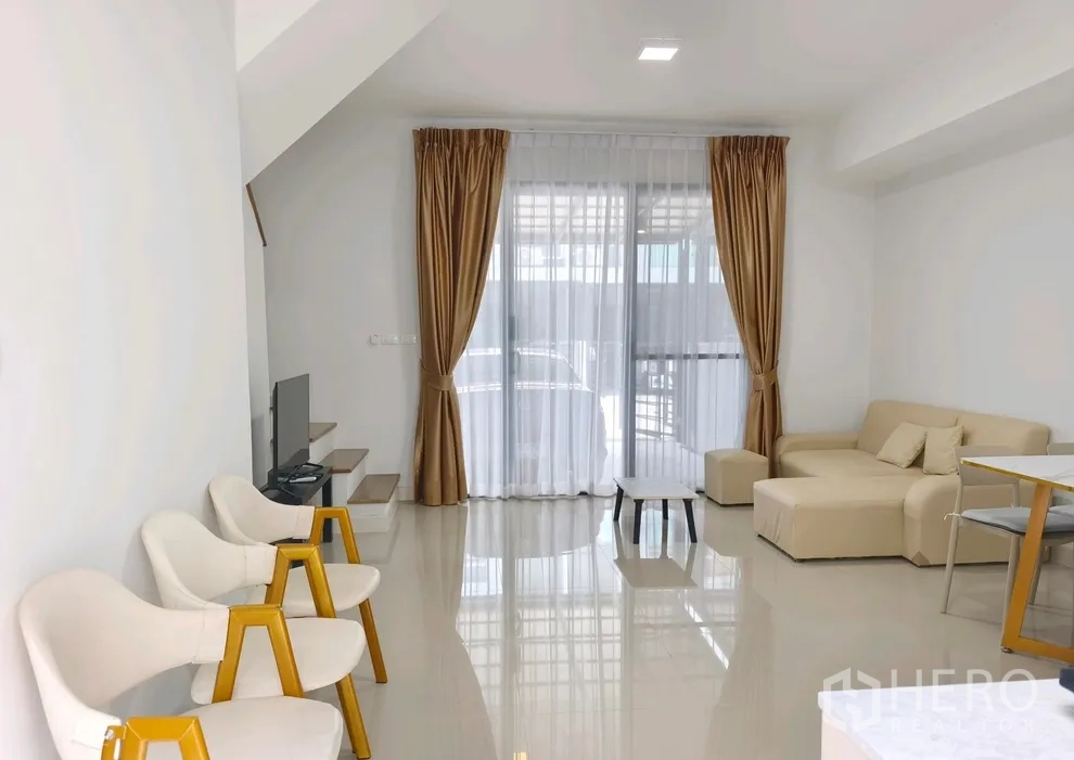 联排别墅 for rent in Bang Phli, Samut Prakan - 客厅配转角沙发、电视与通向车棚的落地窗帘。