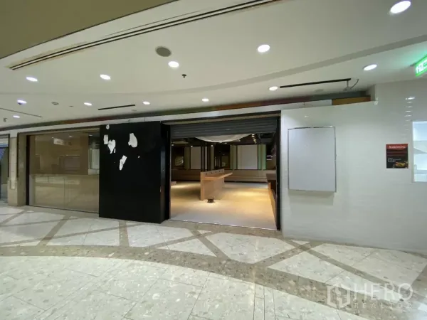 Retail Space for rent - Open entrance with roller shutter revealing retail interior, counters and ceiling lighting.