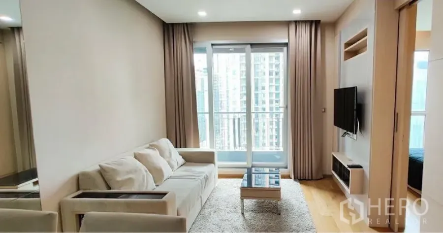 公寓 出租在Ratchathewi, Bangkok - 明亮客厅，设沙发、壁挂电视与阳台，可眺望曼谷天际线。