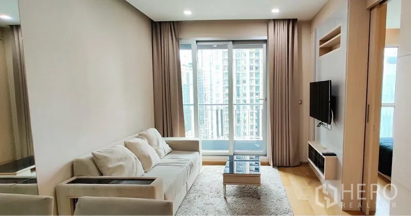 公寓 出租在Ratchathewi, Bangkok - 明亮客厅，设沙发、壁挂电视与阳台，可眺望曼谷天际线。