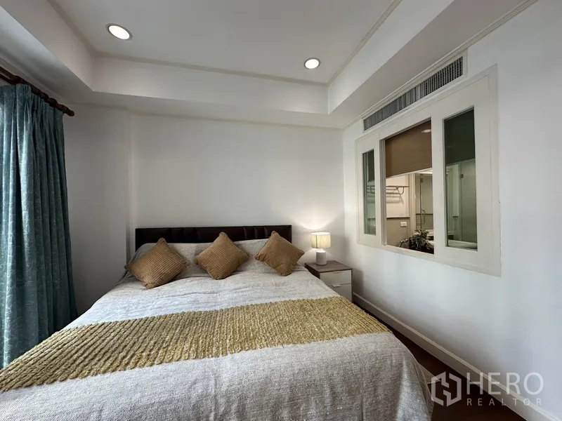 คอนโด ให้เช่า - ห้องนอนหลักฝ้าหลุม โคมไฟข้างเตียง และหน้าต่างภายในมองไปยังพื้นที่ตู้เสื้อผ้า