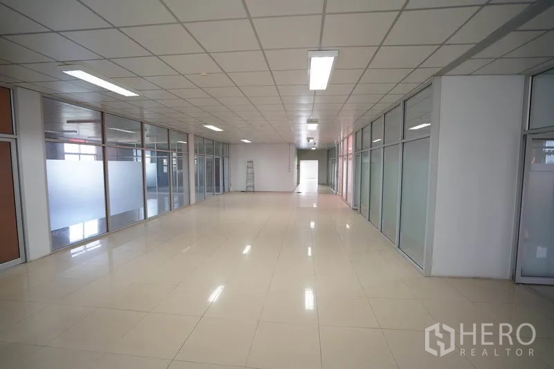 Factory for sale in Khlong Luang, Pathum Thani - Long corridor lined with glass offices and polished tile flooring.