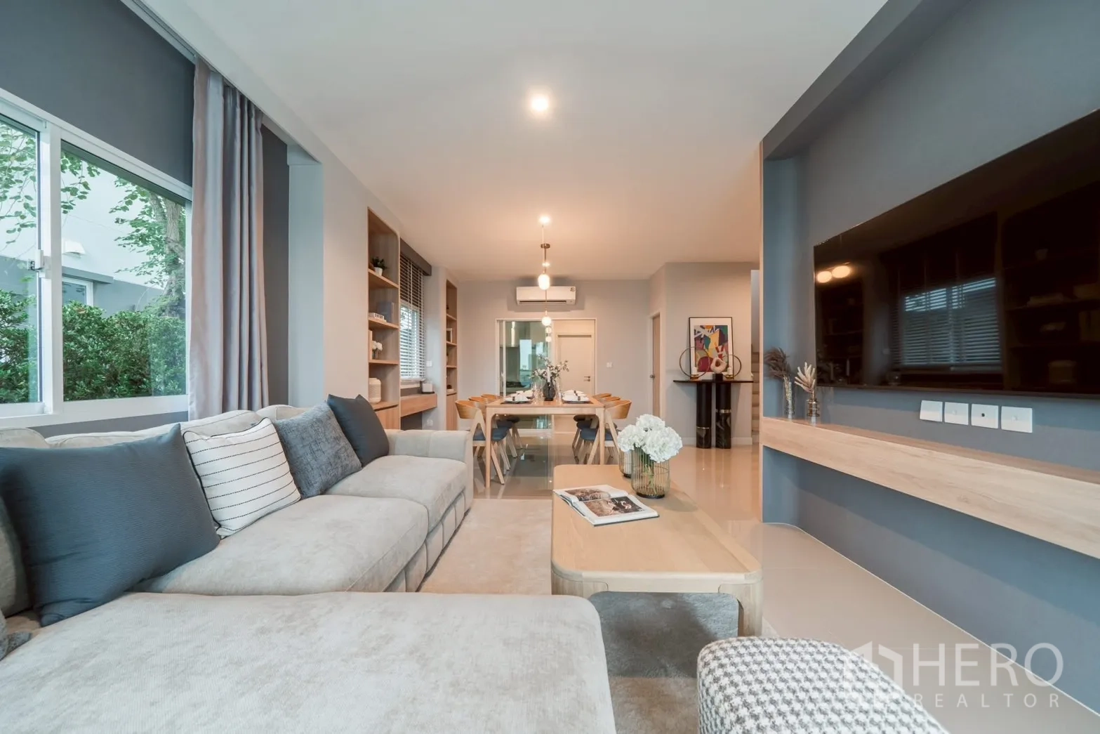 Detached House for rent in Saphan Sung, Bangkok - Open‑plan living and dining room with large sectional sofa, TV wall and warm lighting.