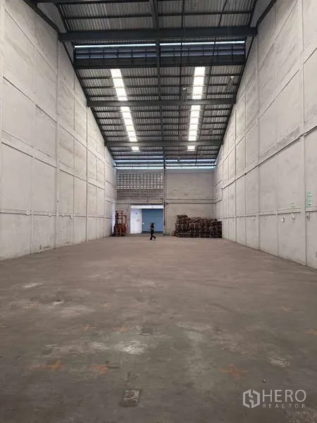 Warehouse for rent in Mueang Samut Prakan, Samut Prakan - Empty high-clearance warehouse hall with concrete floor and skylights.