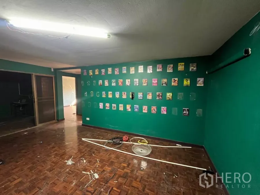 Shophouse for rent in Watthana, Bangkok - Spacious room with green walls, parquet floor and decorative prints, with a sliding door to another area.