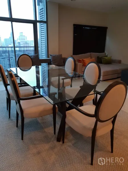 Condominium for rent in Khlong Toei, Bangkok - Dining area with a glass-top table and six upholstered chairs beside floor-to-ceiling windows.