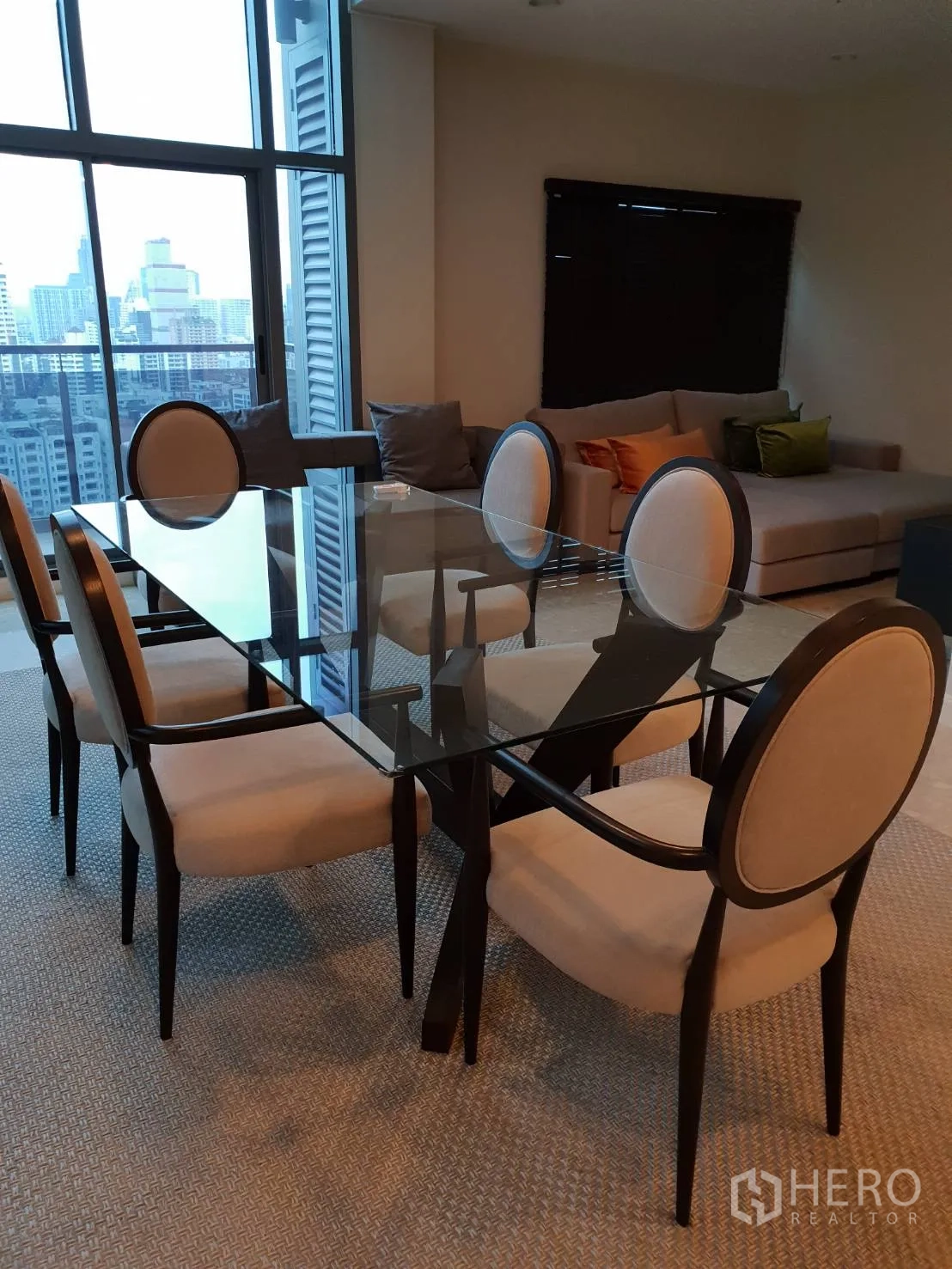 Condominium for rent in Khlong Toei, Bangkok - Dining area with a glass-top table and six upholstered chairs beside floor-to-ceiling windows.