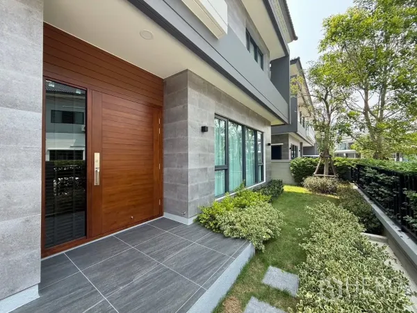 独立式住宅 出租在Bang Phli, Samut Prakan - 木质大门与瓷砖门廊，旁边为修剪整齐的前花园