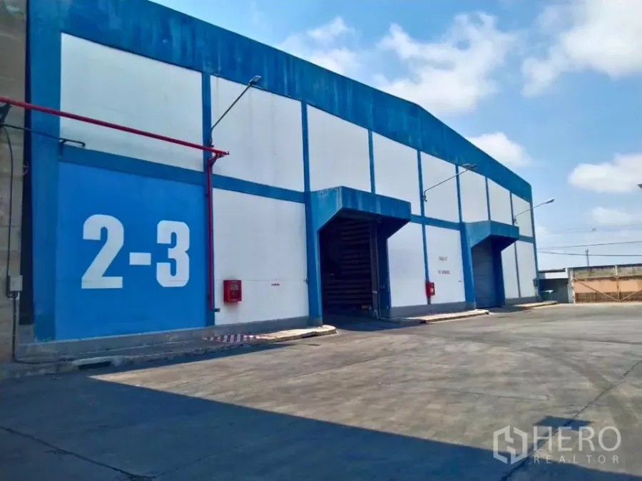 工厂 出租在Samut Prakan - 蓝白色工厂外观，卷帘门装卸月台与宽阔卡车通道。