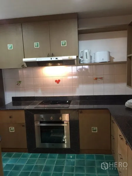 Condominium for rent in Watthana, Bangkok - U-shaped kitchen with electric cooktop, oven, tiled backsplash and green tiled floor.