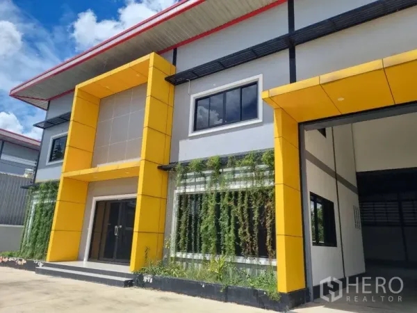 Warehouse for rent or sale in Krathum Baen, Samut Sakhon - Front elevation of two-story warehouse with striking yellow frames, glass entrance and landscaped green wall.