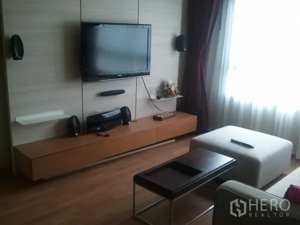 Condominium for rent in Khlong San, Bangkok - Living area media wall with mounted TV, floating cabinet, speakers and an ottoman by the window.