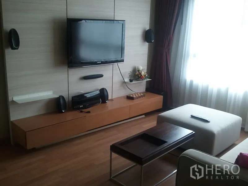 Condominium for rent in Khlong San, Bangkok - Living area media wall with mounted TV, floating cabinet, speakers and an ottoman by the window.
