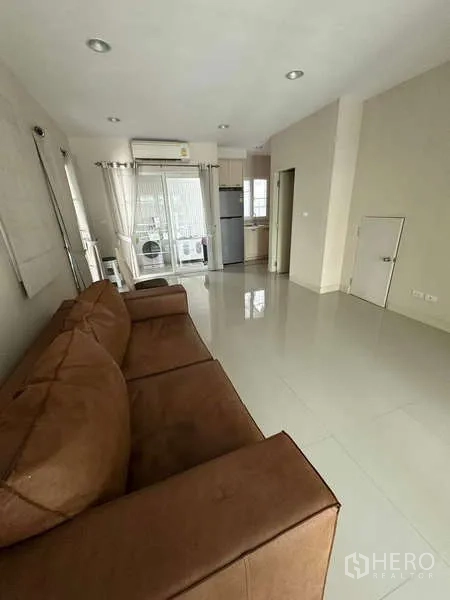 联排别墅 出租或出售在Wang Thonglang, Bangkok - 开放式客厅，棕色沙发、亮面地砖，连通厨房和洗衣区。