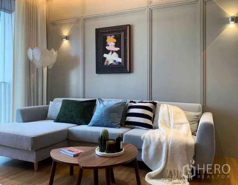 Condominium for rent or sale in Watthana, Bangkok - Cozy lounge with L-shaped sofa, cushions, round coffee table and wall sconces.
