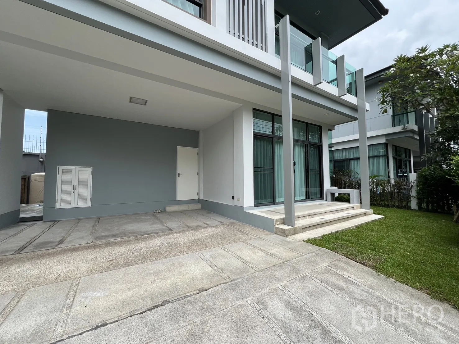 Detached House for rent in Bang Kapi, Bangkok - Carport beside floor-to-ceiling windows and small front steps with a neat lawn.
