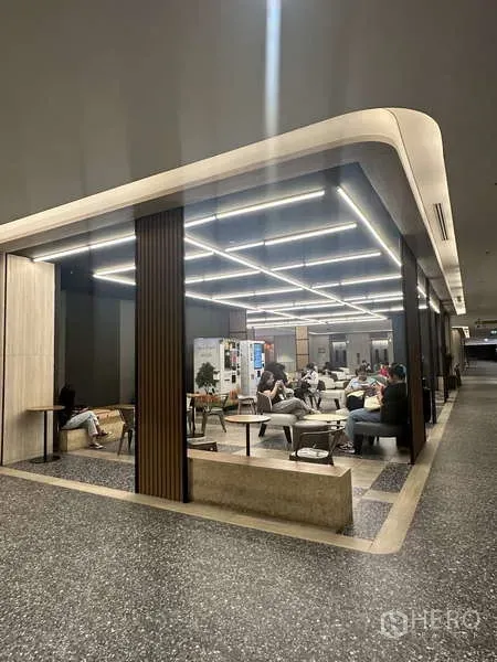 Retail Space for rent - Glass-partitioned retail seating zone with grid LED lighting, sofas and wood-slat columns along a wide corridor.