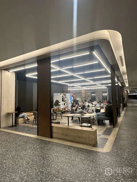 Retail Space for rent - Glass-partitioned retail seating zone with grid LED lighting, sofas and wood-slat columns along a wide corridor.