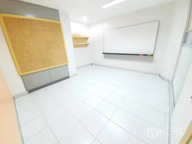 Office Space for rent in Bang Na, Bangkok - Workspace with a cork pinboard, wall shelves and whiteboard on tiled flooring.