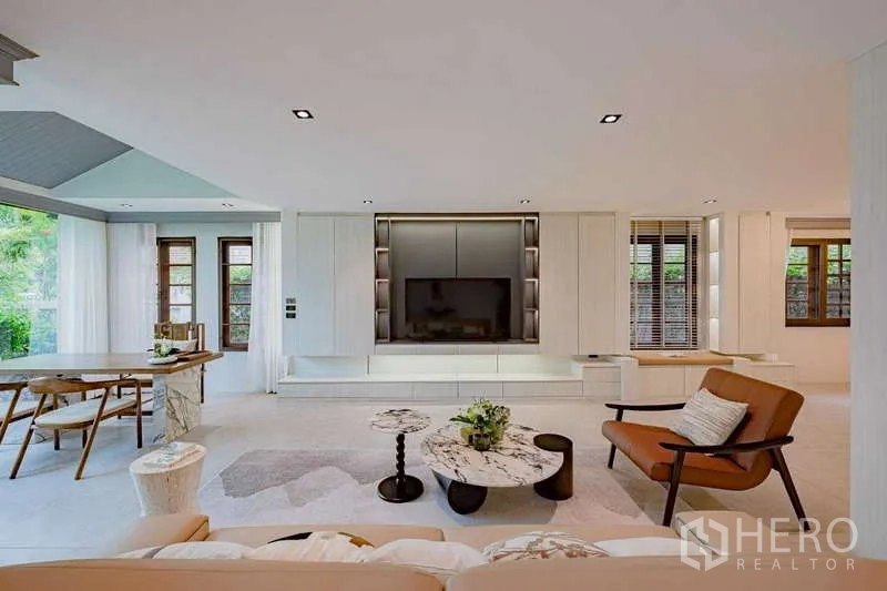 Detached House for rent or sale in Phra Khanong, Bangkok - Light-filled living room with built-in TV wall, marble coffee tables, and garden views.