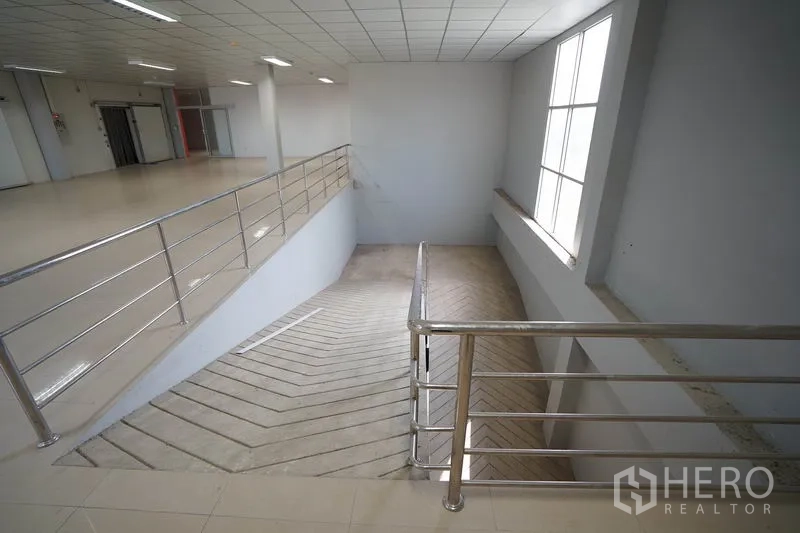 Factory for sale in Khlong Luang, Pathum Thani - Internal ramp with stainless handrails linking floors, lit by a large window.
