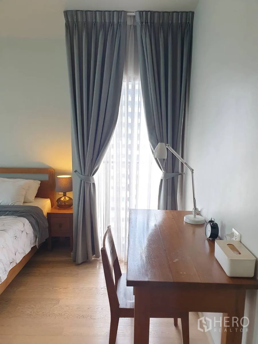 公寓 出租或出售在Bangkok - 卧室书桌与椅子紧邻带窗帘的落地窗。