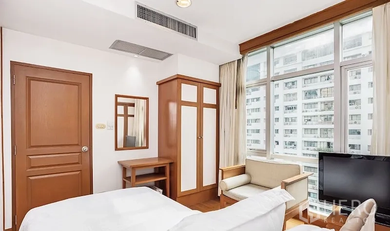 公寓 出租在Pathum Wan, Bangkok - 卧室一角配衣柜、扶手椅、电视和大窗，俯瞰城市景观。