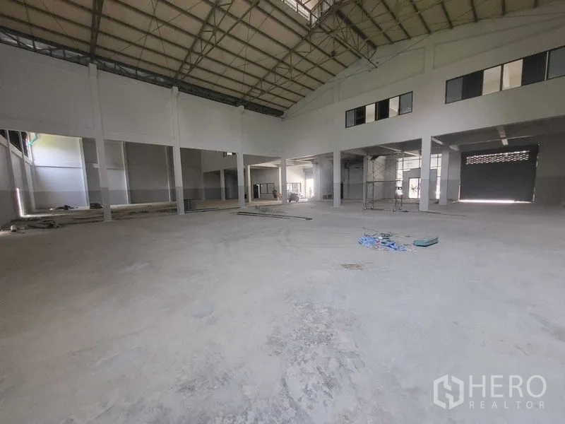 Factory for rent or sale in Samut Prakan - High-clearance warehouse area with loading bay roller shutter and mezzanine windows.