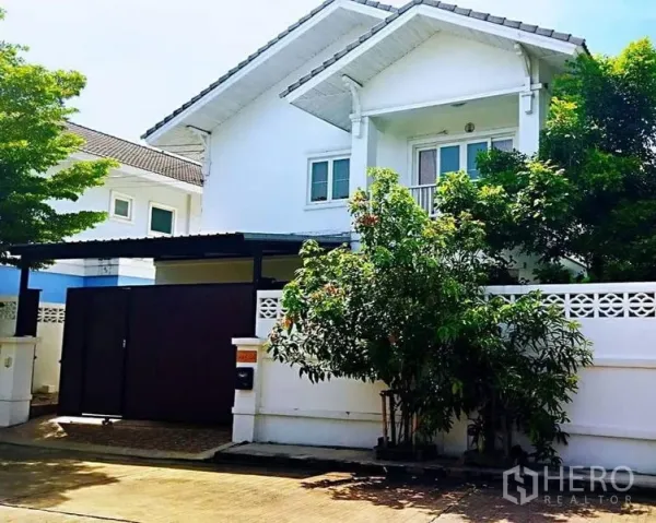 Detached House for sale in Sai Mai, Bangkok - Front exterior of a white two-storey detached house with balcony, trees and gated entrance.