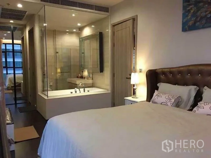 Condominium for rent in Watthana, Bangkok - Cozy bedroom with an upholstered headboard and a glass-partition bathroom featuring a tub.