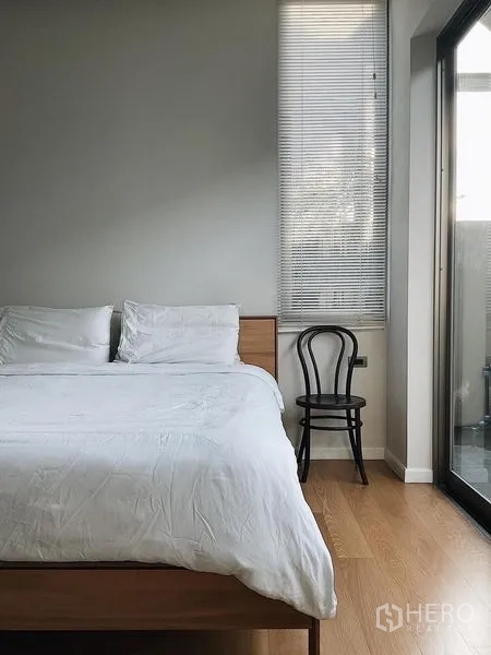 Detached House for sale in Bang Kapi, Bangkok - Cozy bedroom with white bedding, wood floor, and sliding door to a balcony.