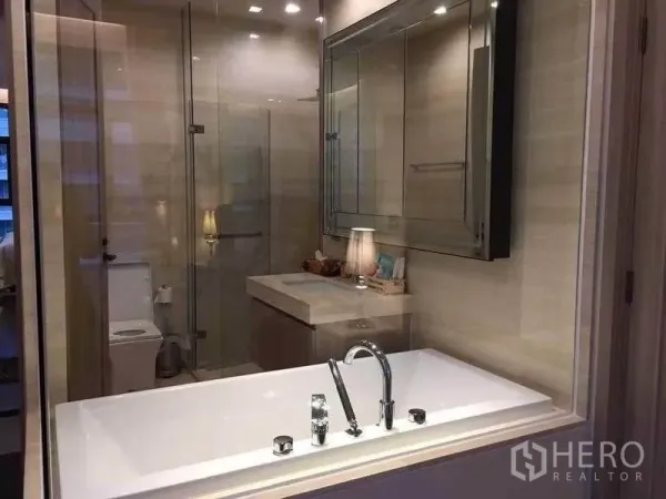 Condominium for rent in Watthana, Bangkok - Glass-walled bathroom with soaking tub, vanity, and a separate shower beside the toilet.