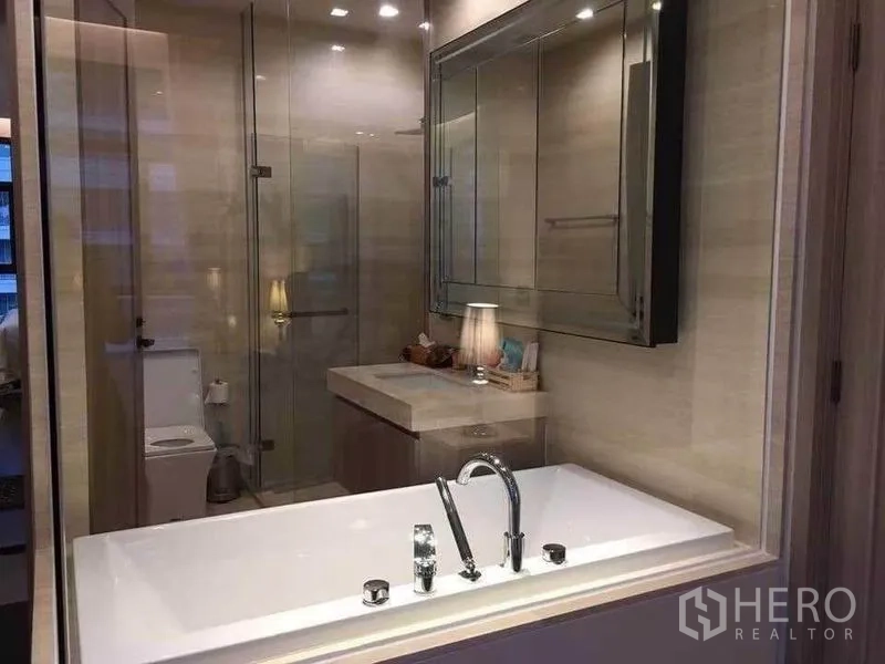 Condominium for rent in Watthana, Bangkok - Glass-walled bathroom with soaking tub, vanity, and a separate shower beside the toilet.