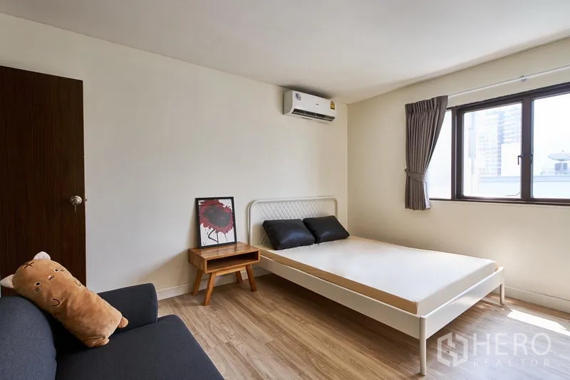 Condominium for rent in Watthana, Bangkok - Sunlit guest bedroom with double bed, city-facing window and curtains.